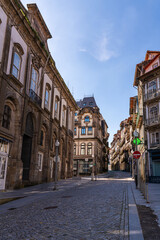 Fototapeta premium Historic narrow street in Porto Portugal lined with traditional tiled buildings and balconies. Sunny day with clear blue sky creating depth perspective and authentic European city atmosphere.