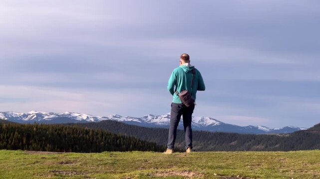 Man with camera bag trekking in mountains, scouting location for landscape photography in open countryside. Travel footage for adventure, discovery, recreation, and nature storytelling concepts