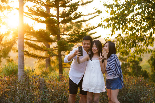 Happy Asian Family Taking Selfie Together in Nature at Golden Hour