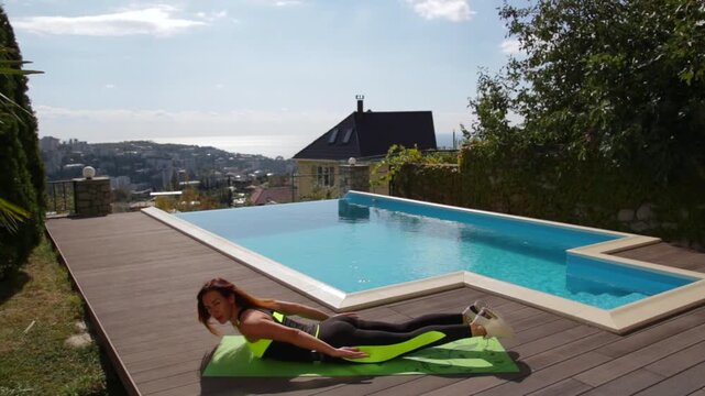 Athletic fitness girl practicing prone back extension superman hyper-extension exercise on green yoga mat at wooden terrace deck
