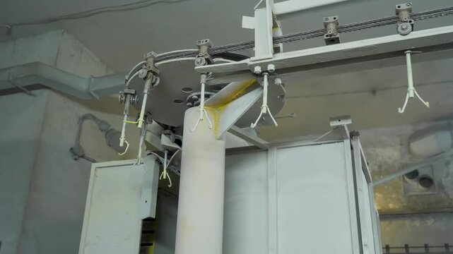 Automated overhead conveyor mechanism moves metal hooks along ceiling track inside industrial facility for specialized powder surface finishing processes