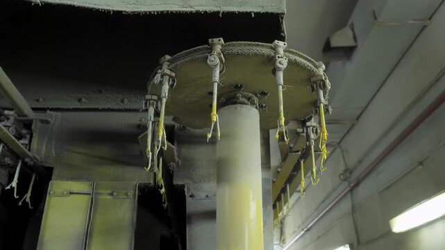 Rotating mechanism featuring multiple suspended metal hangers moves continuously inside an industrial powder coating chamber