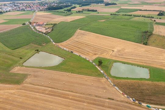 Aerial view of the Open Beatz Festival traffic queue on a rural road passing through agricultural fields and ponds near Herzogenaurach, Bayern, Germany.