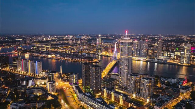 Aerial timelapse of a modern metropolis skyline at night with an illuminated bridge and river traffic