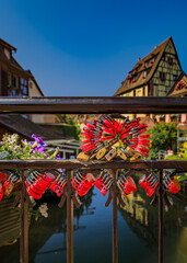 Obraz premium Red love locks hang on a bridge railing overlooking a scenic Lauch River canal running through Little Venice, the old town district in Colmar, France