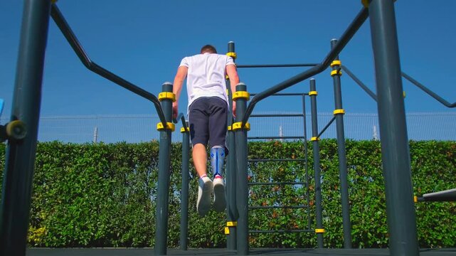 Athlete with a prosthetic leg doing triceps dips on parallel bars outdoors