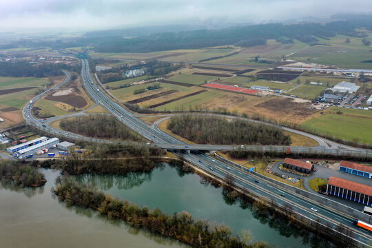 Aerial view of a highway interchange with traffic, surrounding agricultural fields, and a river under an overcast sky in Forchheim, Bavaria, Germany.