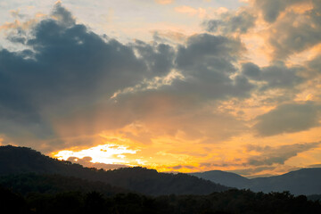 Obraz premium Clouds fill sky above mountain range during sunset. colors change as daylight fades. scene shows transition from day to night with dramatic light. Clouds gather in the sky, evening light