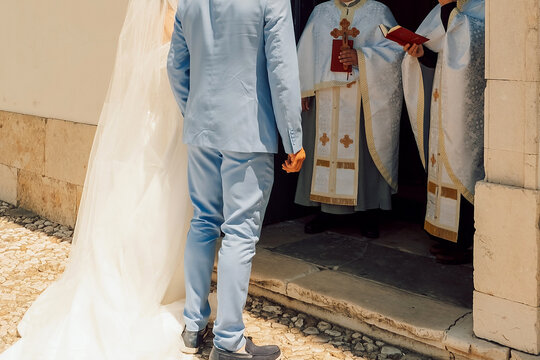 Couple prepares for wedding ceremony at church with officiant and attendees present on sunny day. groom wears a suit and the bride is in a wedding dress. An officiant is present with attendees.