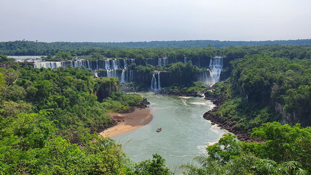 Panoramic view of Iguazu Falls with a tourist boat navigating the canyon river surrounded by lush rainforest.