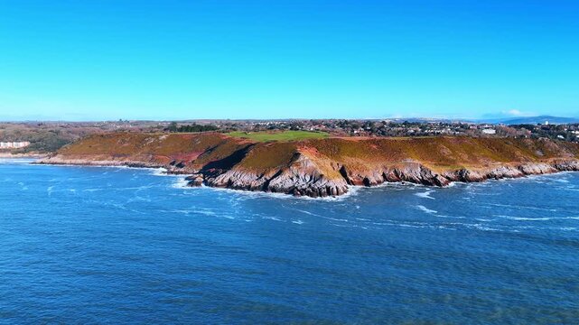 Aerial View of Coastal Promontory with Distant Lighthouse Islet. A wooded promontory extends toward small rocky islets with a lighthouse as the bay opens to a misty far shore.