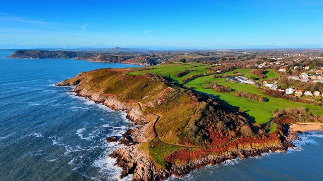 Wide Aerial View of Welsh Coastline with Headlands and Open Sea. A sweeping coastline of rocky headlands and green slopes recedes into the distance beneath a clear blue winter sky.