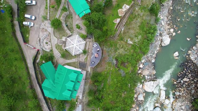 Aerial drone view straight down of a riverside villa surrounded by lush green mountains and forest landscape near beas parvati river in the scenic Manali region of Himalayas.