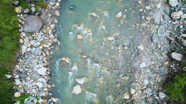 aerial drone shot rising shooting straight down on rapidly flowing water of parvati beas river filled with stones surrounded by trees showing the cool fresh waters of Indian hill stations