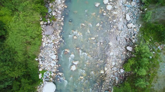 aerial drone shot straight down on rapidly flowing water of parvati beas river filled with stones surrounded by trees showing the cool fresh waters of Indian hill stations
