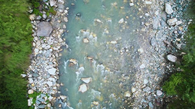 aerial drone shot descending straight down on rapidly flowing water of parvati beas river filled with stones surrounded by trees showing the cool fresh waters of Indian hill stations