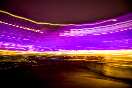 Abstract long exposure light trails with vibrant purple and golden yellow neon streaks on a dark background