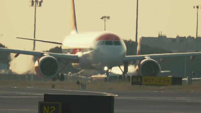 Airplane taxiing at sunset on busy runway in airport setting with bright lights and clear sky