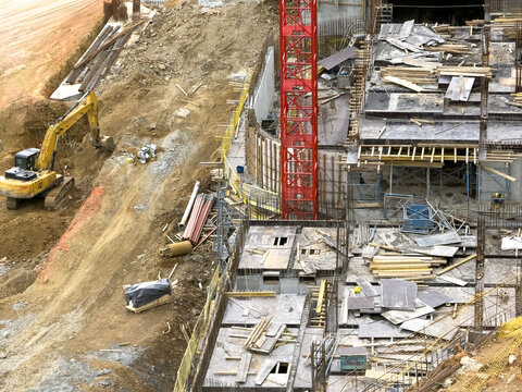 Aerial view of a busy construction site featuring a yellow excavator, a red tower crane, and concrete foundations in Sariyer, Istanbul, Turkiye.