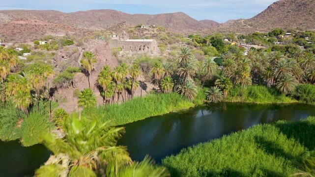 Explore the Mission of Santa Rosalia in Mulege Baja California Sur, Mexico, with views of desert mountains and lush oasis under afternoon light.
