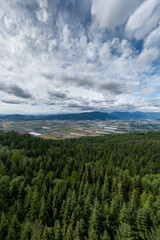 Obraz premium Aerial View of Fraser Valley Farmland and Forest With Mountains Under Dramatic Cloudy Sky, British Columbia