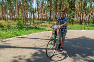 Naklejka premium Dad rides his daughter in a bicycle seat in forest. A man carries a small child on a bicycle.