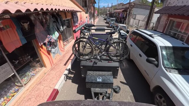 Teardrop camper trailer is towed along narrow streets in Mulege Baja California Sur Mexico while passing local shops and cars.