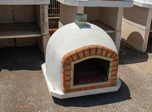 Outdoor dome pizza oven made of refractory clay and concrete with brick arch entryway in a garden setup