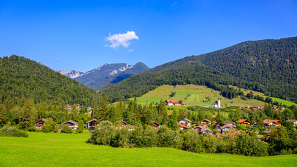 Naklejka premium Mountains frame a small village in a green valley under a clear blue sky during daytime in summer