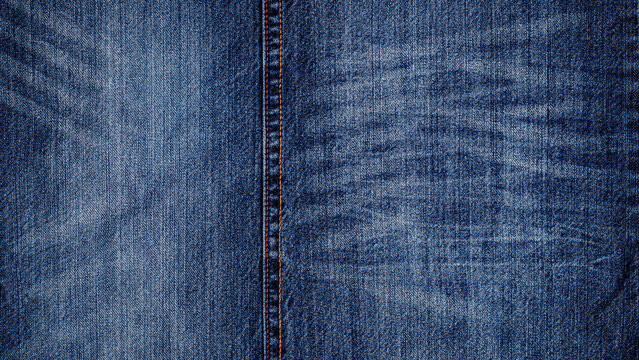 Close view of faded blue denim fabric showing texture and patterns of wear and tear in natural light during daytime
