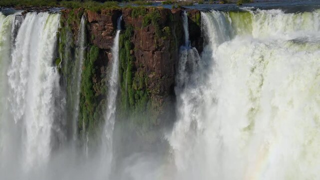 Majestic waterfalls of Iguazu cascading over a vertical cliff with vibrant green plants growing on wet rocks, a breathtaking natural wonder located on the border of Argentina and Brazil