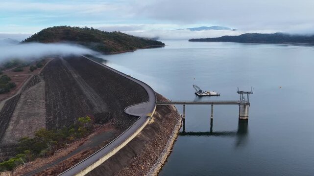 Aerial video showcasing the Glenbawn Dam wall surrounded by a foggy landscape in the Upper Hunter region of NSW Australia. Low clouds and mist drift across the expansive reservoir