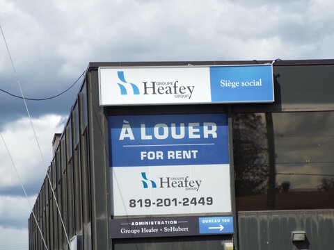 Gatineau, Quebec, Canada &ndash; April 21, 2026: An office building corner displays "Groupe Heafey Group" signage along with a large blue and white "&Agrave; LOUER FOR RENT" commercial banner on Boulevard Saint-Jo