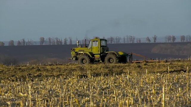 Tractor driving across a field in autumn while harrowing the soil after harvest. Concept of seasonal agricultural work, soil cultivation, and preparation of farmland for future crops. Modern farming