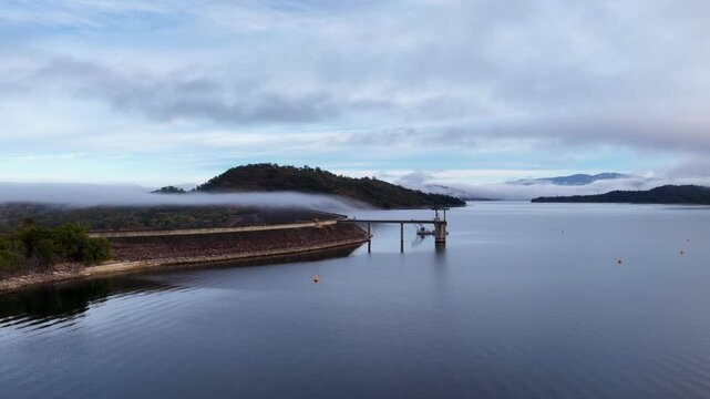 Aerial video showcasing the Glenbawn Dam wall surrounded by a foggy landscape in the Upper Hunter region of NSW Australia. Low clouds and mist drift across the expansive reservoir