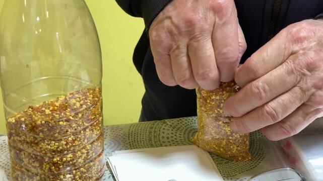 Close-up white male salesman packing bee pollen into transparent bag, hands pressing and sealing pouch on table with yellow