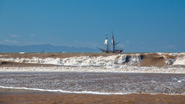 Wooden tall ship which is a full-scale 18th-century brig replica sailing through white-capped waves along the California coastline near Ventura, United States