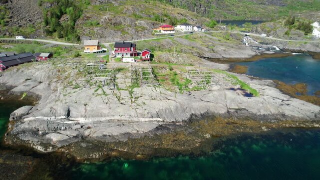 Aerial drone flying over a typical Norwegian fishing village with traditional red rorbu huts and wooden racks for drying stockfish. Lofoten islands.