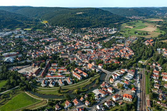 Aerial view of Ebermannstadt town center with red-roofed houses, the Wiesent river, and lush green hills under a clear sky Ebermannstadt, Bavaria, Germany.