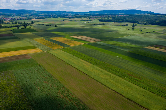 Aerial view of patchwork agricultural fields with green and yellow crops under a cloudy sky with rolling hills in the distance Forchheim, Bavaria, Germany.