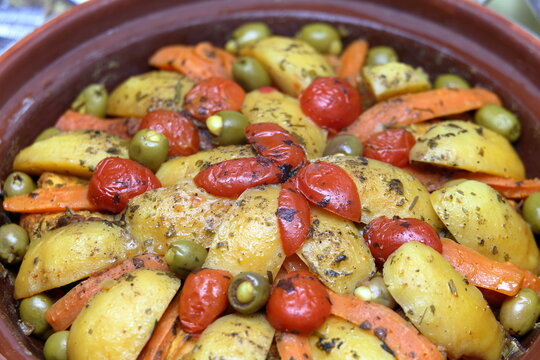 Macro close-up of a traditional Moroccan vegetable tagine with potatoes, carrots, tomatoes, and green olives