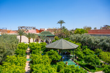 Fototapeta premium Visitors enjoy the beauty of Secret Garden in Marrakesh. The garden features palm trees, green plants, and pathways for people to stroll. It is a popular spot for relaxation and conversation.
