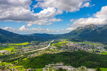 Fototapeta premium Aerial view shows the district town of Reutte in Tyrol, Austria. Green fields and mountains surround the town. Clouds float in the sky during daytime.