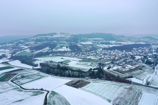 Aerial view of the Walberla mountain overlooking snow-covered fields and the village of Kirchehrenbach, Bavaria, Germany.