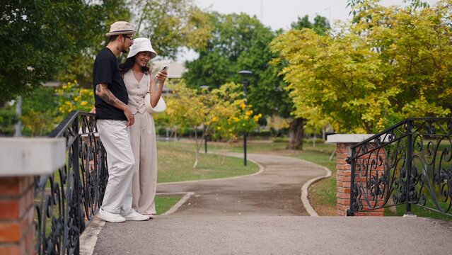 Couple standing on park bridge, smiling and interacting with smartphone
