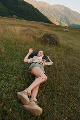 Fototapeta premium Smiling woman lying in a grassy field with mountains in the distance, enjoying a sunny outdoor moment. Casual, relaxed lifestyle in nature, showcasing freedom, comfort, and a connection to wide