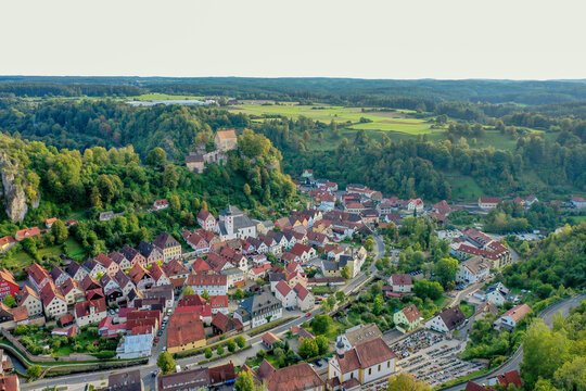 Aerial view of Pottenstein Castle overlooking the historic town with red-roofed houses and lush green hills in Pottenstein, Bavaria, Germany.