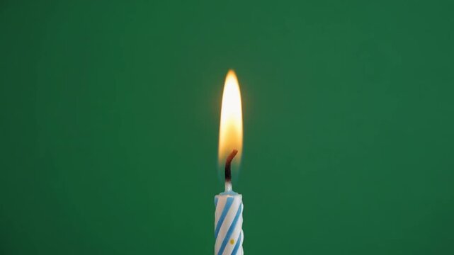 Close-up of a single burning birthday candle with a blue and white striped pattern on a plain green background, perfect for celebrations