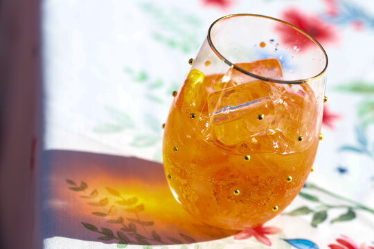 Tropical cocktail in a wine glass. The cold refreshment is orange and is filled with ice cubes. The color is orange. The alcohol beverage is tasty and refreshing on a hot summer day. 