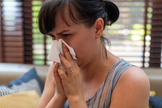 Woman sneezing with tissue indoors.